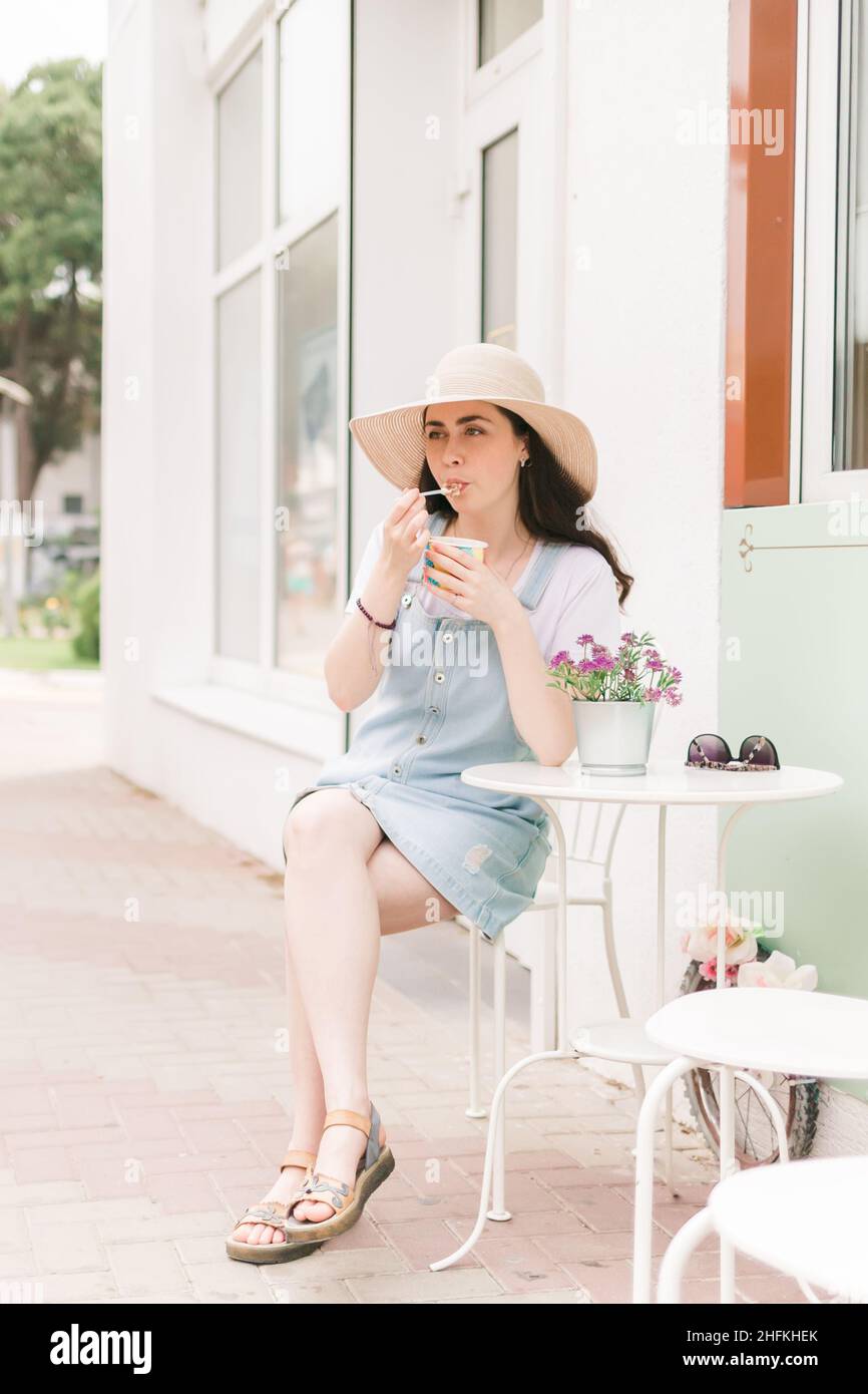 Estate. Bella giovane donna seduta in un caffè di strada e gusto gelato. Orientamento verticale. Foto Stock