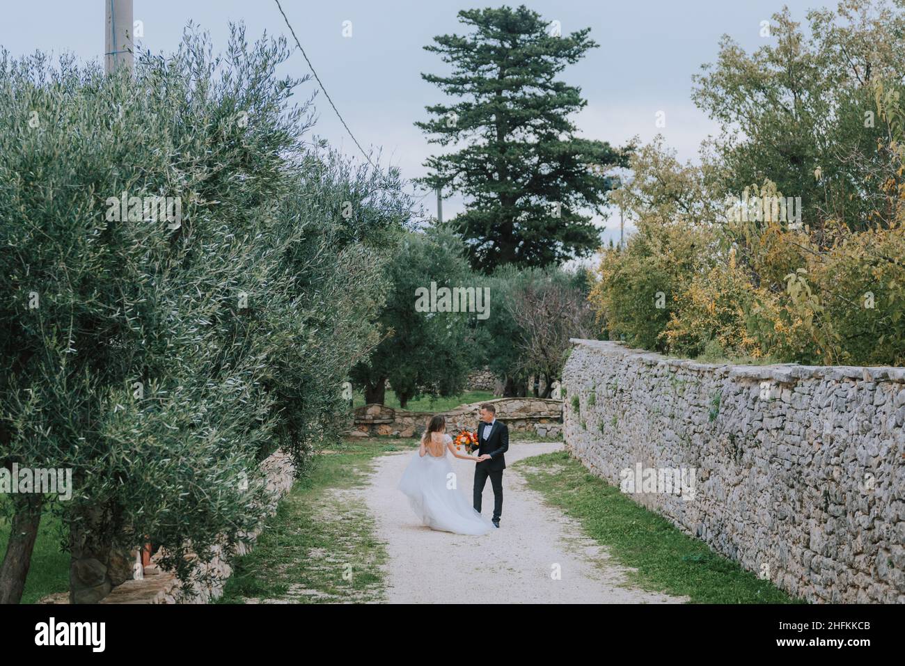 Felice coppia sorridente di stile che cammina in Toscana, Italia il giorno del matrimonio. La sposa e lo sposo camminano lungo la strada per le mani. Un giovane di stile Foto Stock