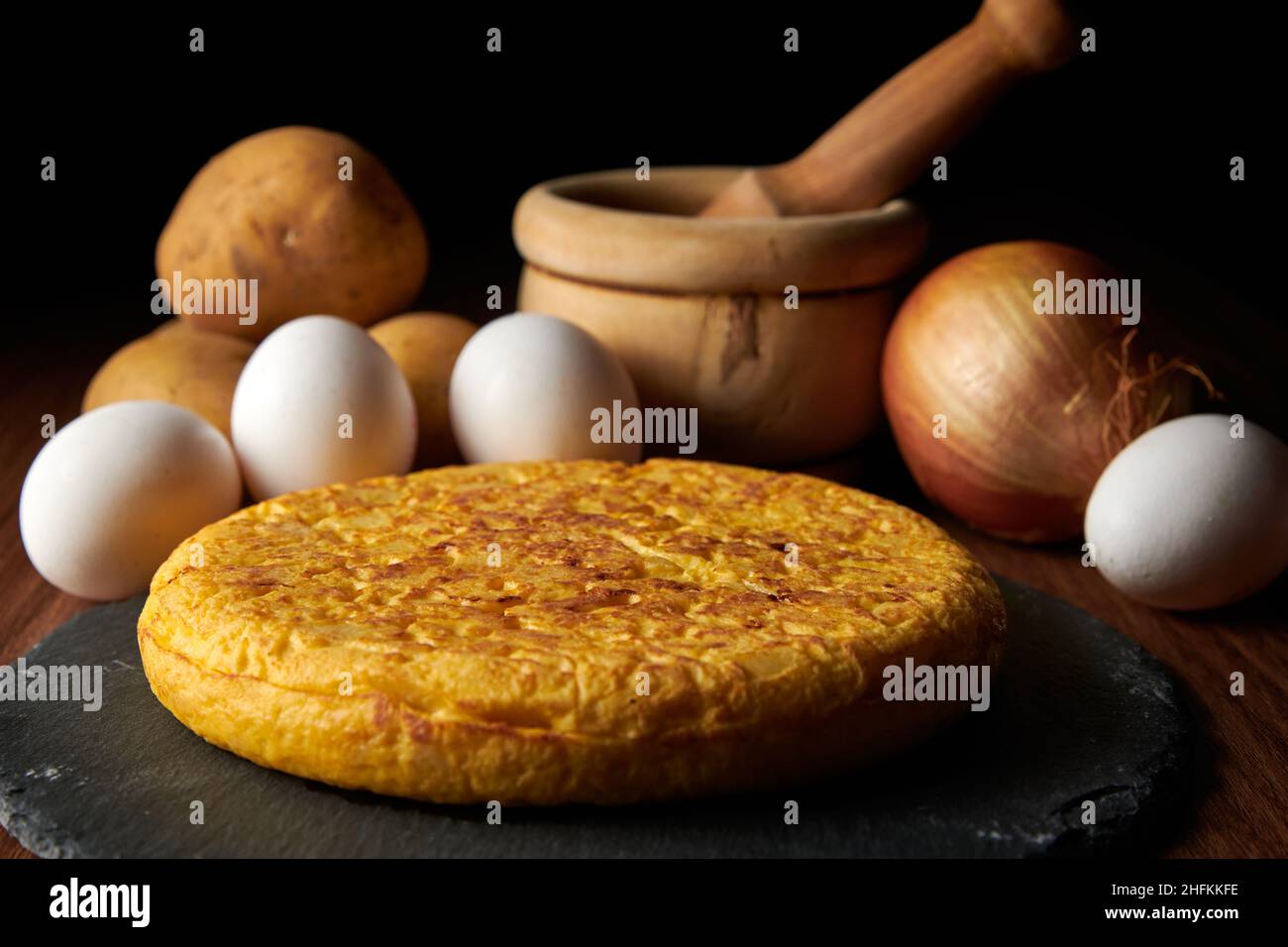 Un primo piano di una fresca e gustosa frittata spagnola e gli ingredienti sullo sfondo, un piatto tradizionale spagnolo Foto Stock