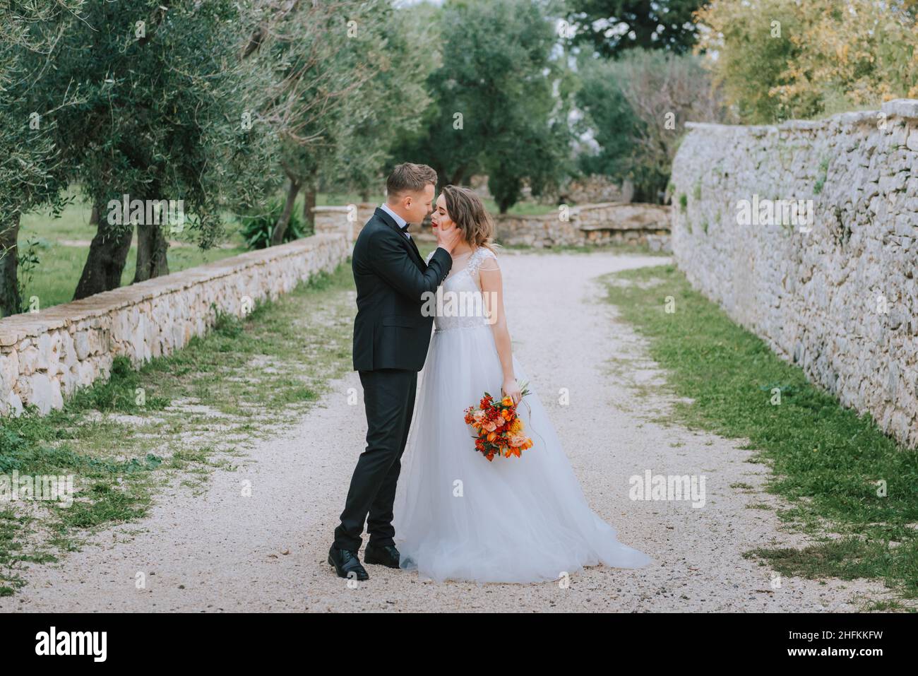 Felice coppia sorridente di stile che cammina in Toscana, Italia il giorno del matrimonio. La sposa e lo sposo camminano lungo la strada per le mani. Un giovane di stile Foto Stock