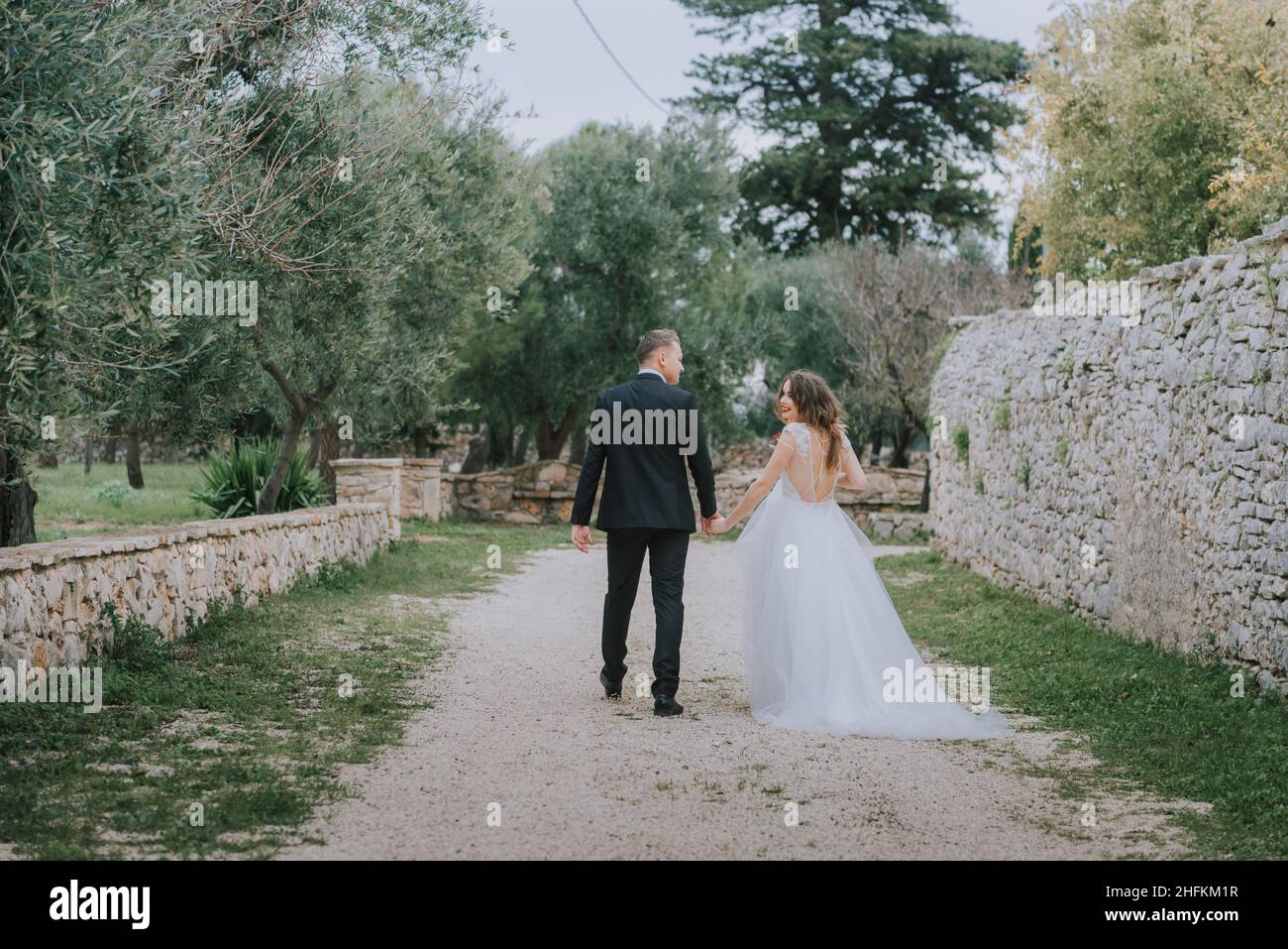 Felice coppia sorridente di stile che cammina in Toscana, Italia il giorno del matrimonio. La sposa e lo sposo camminano lungo la strada per le mani. Un giovane di stile Foto Stock