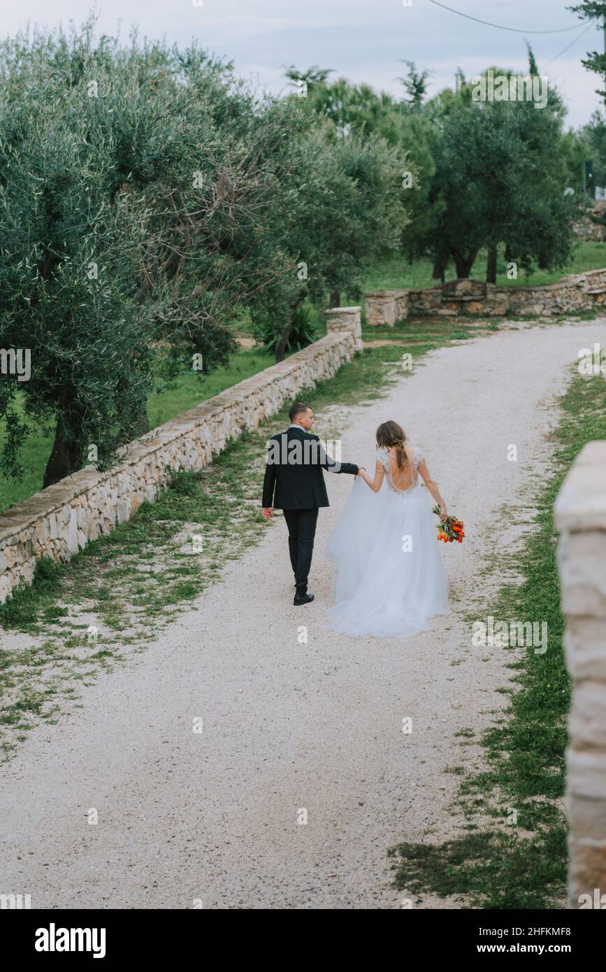 Felice coppia sorridente di stile che cammina in Toscana, Italia il giorno del matrimonio. La sposa e lo sposo camminano lungo la strada per le mani. Un giovane di stile Foto Stock