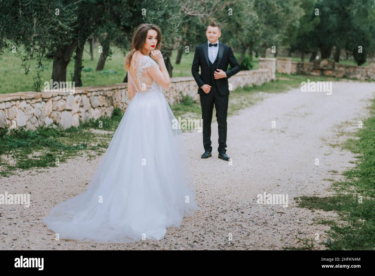 Felice coppia sorridente di stile che cammina in Toscana, Italia il giorno del matrimonio. La sposa e lo sposo camminano lungo la strada per le mani. Un giovane di stile Foto Stock