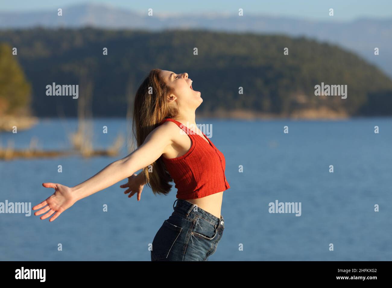 Donna eccitata in rosso urlando per l'aria che stretching braccia in un lago una giornata di sole Foto Stock