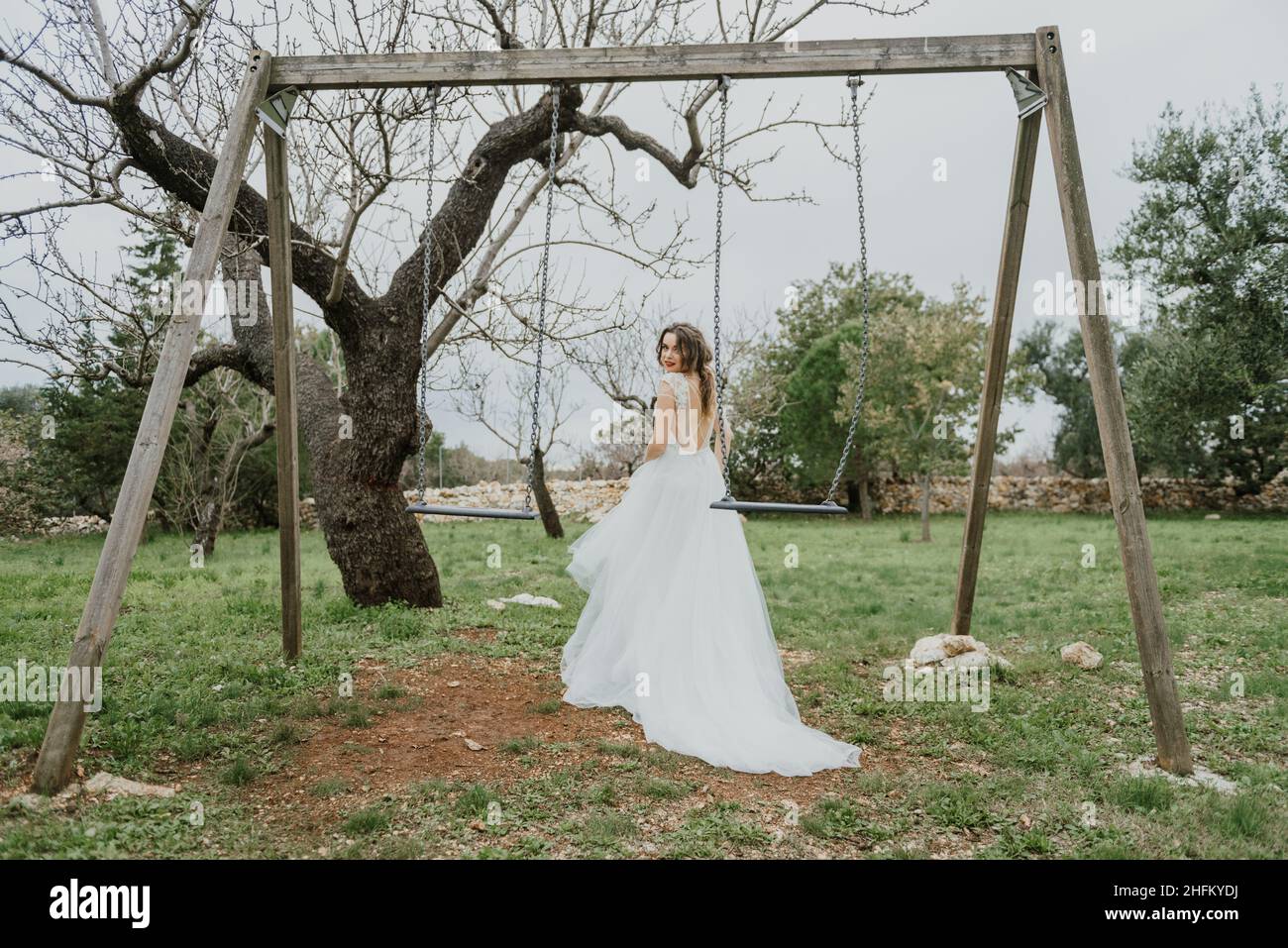 Felice coppia sorridente di stile che cammina in Toscana, Italia il giorno del matrimonio. SPOSI NOVELLI CON L'ALTALENA NEL PARCO. La sposa e lo sposo camminano giù il Foto Stock