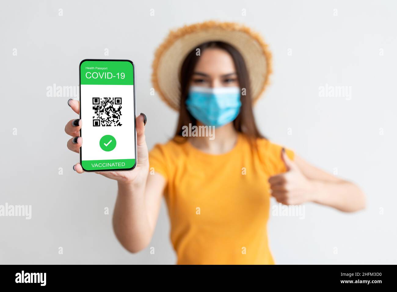 Passaporto sanitario elettronico. Giovane donna che indossa la maschera facciale e lo smartphone con passaporto elettronico digitale in mano Foto Stock