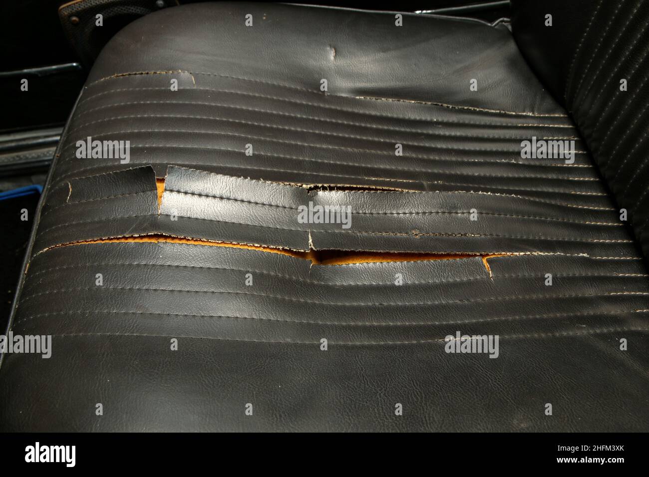 L'interno in pelle artificiale nera della vecchia auto classica che necessita di un rinnovo. Con coprisedile strappato distrutto. Foto Stock