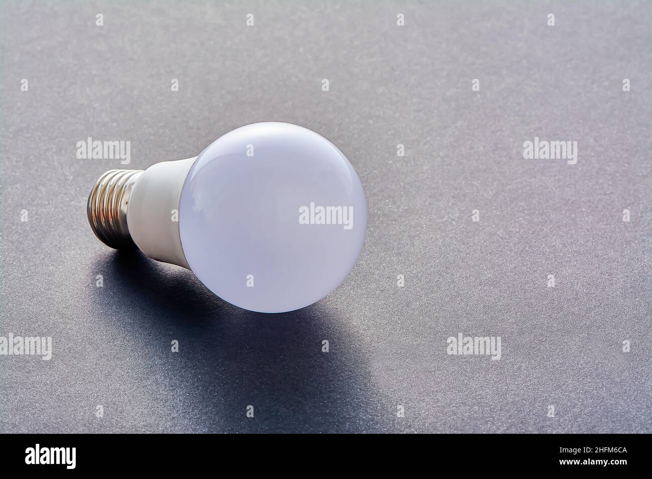Una lampada LED bianca con base E27 giace su uno sfondo grigio Foto Stock