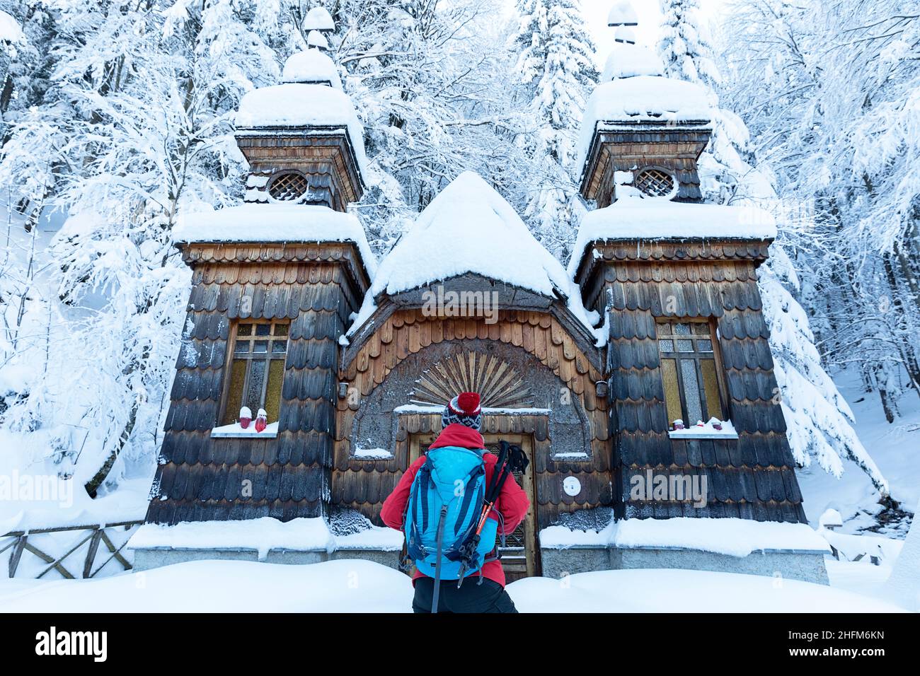 Vista posteriore della donna in abbigliamento invernale e con uno zaino in piedi di fronte alla Cappella russa sul Passo Vršič coperto di neve, Alpi Giulie, Slovenia Foto Stock