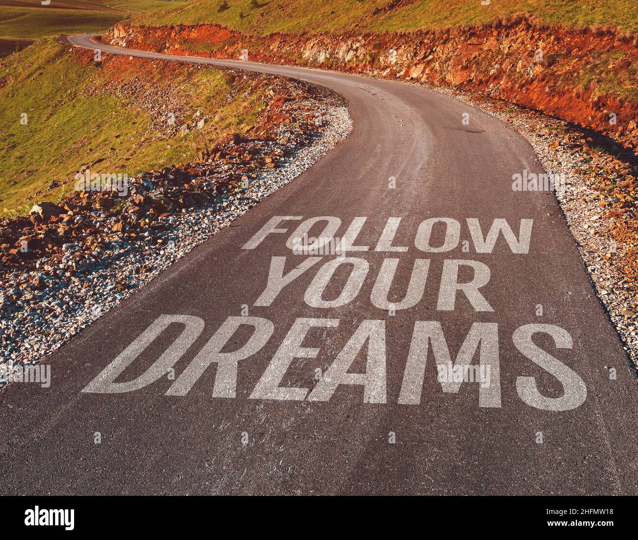 Segui i tuoi sogni messaggio motivazionale sulla strada asfaltata attraverso il paesaggio di campagna, fuoco selettivo Foto Stock