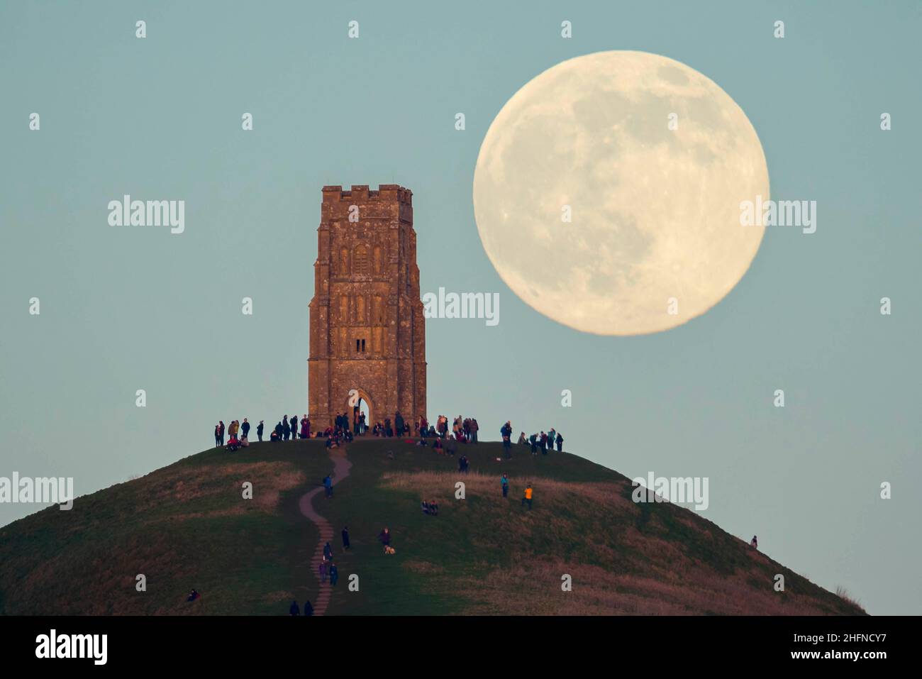 Glastonbury, Somerset, Regno Unito. 17th gennaio 2022. Meteo Regno Unito. La Luna piena del lupo si alza da dietro la St Michael’s Tower su Glastonbury Tor nel Somerset in una fredda serata limpida, mentre le persone si alzano in cima e la guardano crescere. Picture Credit: Graham Hunt/Alamy Live News Foto Stock