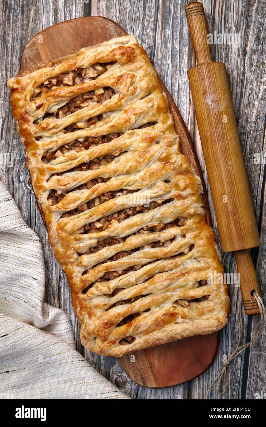 Una torta di strudel di mele in vimini con noci si trova su un tagliere Foto Stock