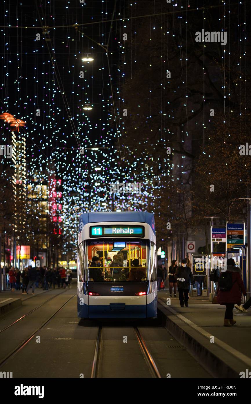 Zurigo, Svizzera - Dicembre 12 2021: Un tram percorre la Bahnhofstrasse, il viale principale del centro di Zurigo con decorazioni natalizie Foto Stock