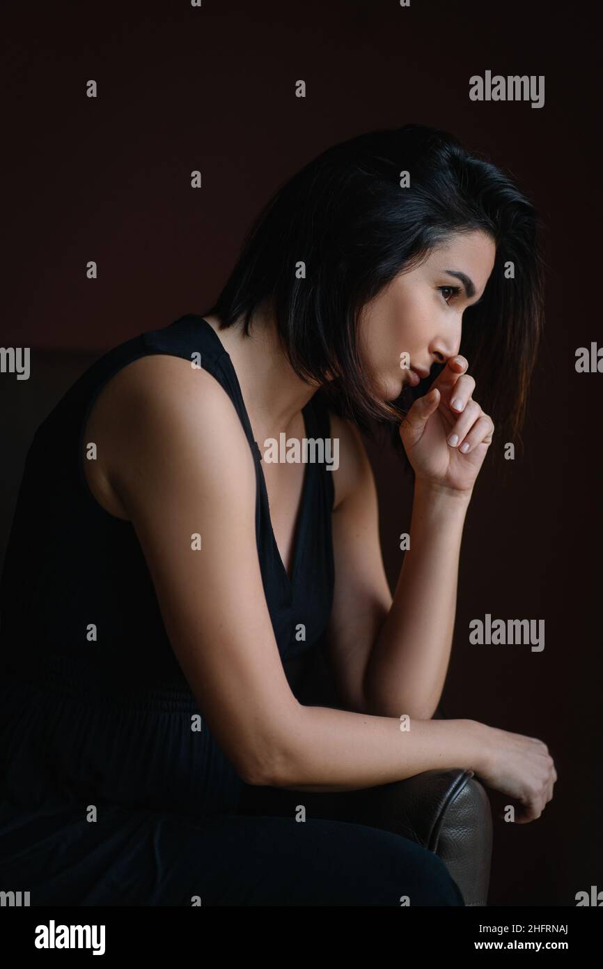 Mediage capelli scuri donna vestito nero sedersi su divano di pelle scuro Foto Stock