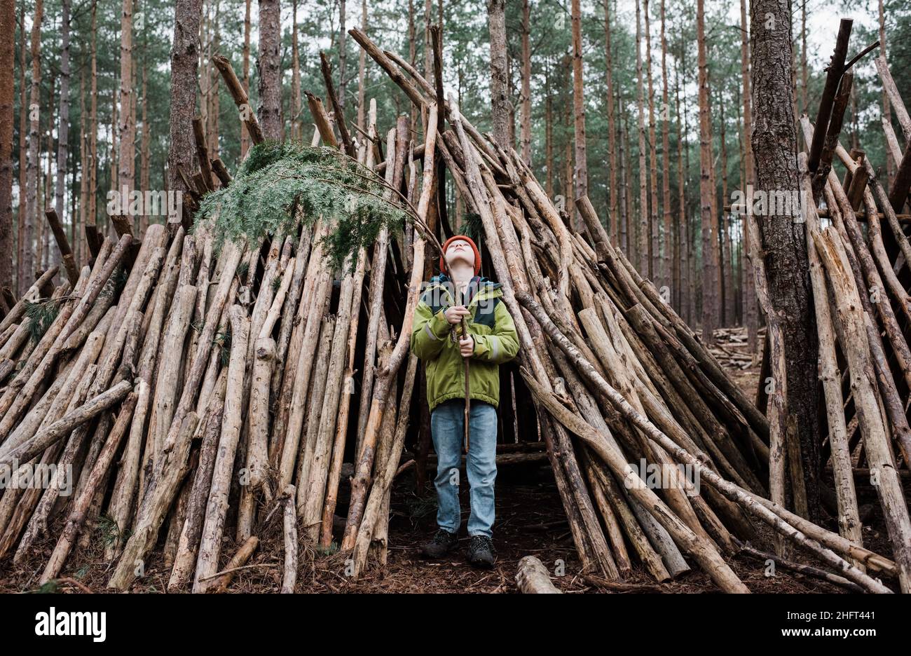 ragazzo costruzione di una casa di alberi nella foresta con tronchi in inverno Foto Stock