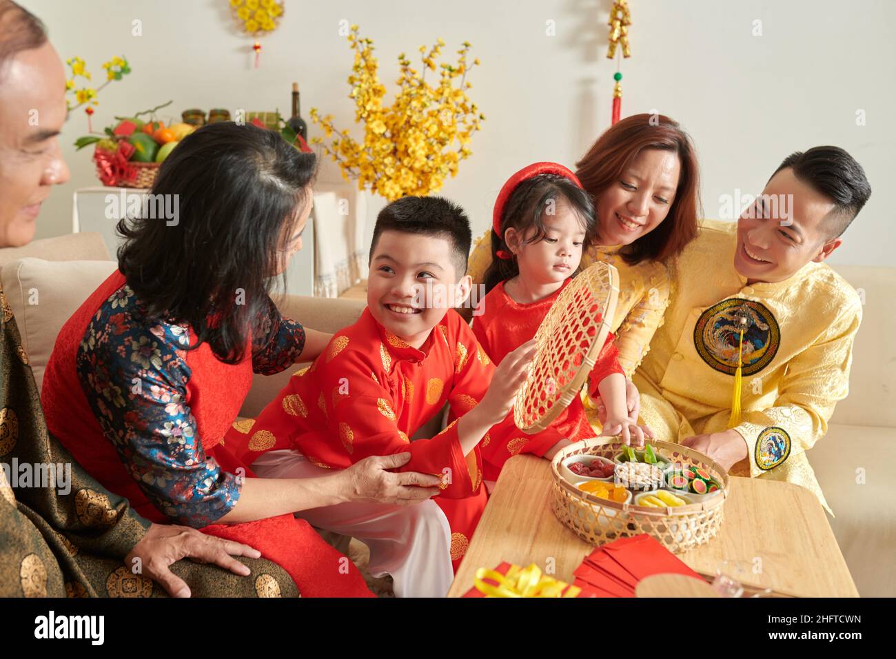 Famiglia felice gustando noci e frutta candita con tè quando festeggia il Capodanno lunare a casa Foto Stock