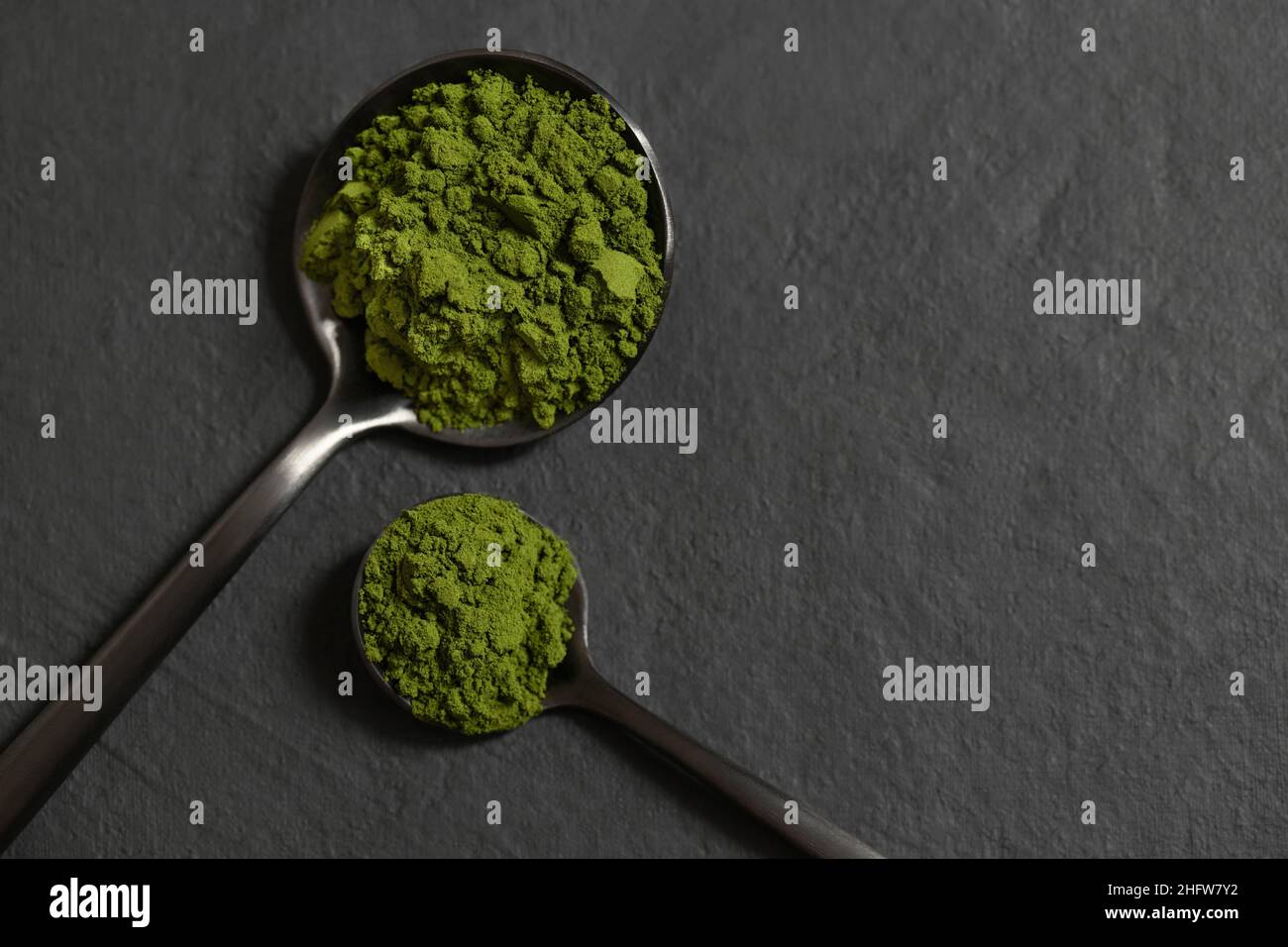 Polvere verde di clorella in cucchiai su sfondo di pietra nera. Spirulina polvere di alghe o orzo. Superfood. Vista dall'alto. Spazio per il testo. Foto Stock