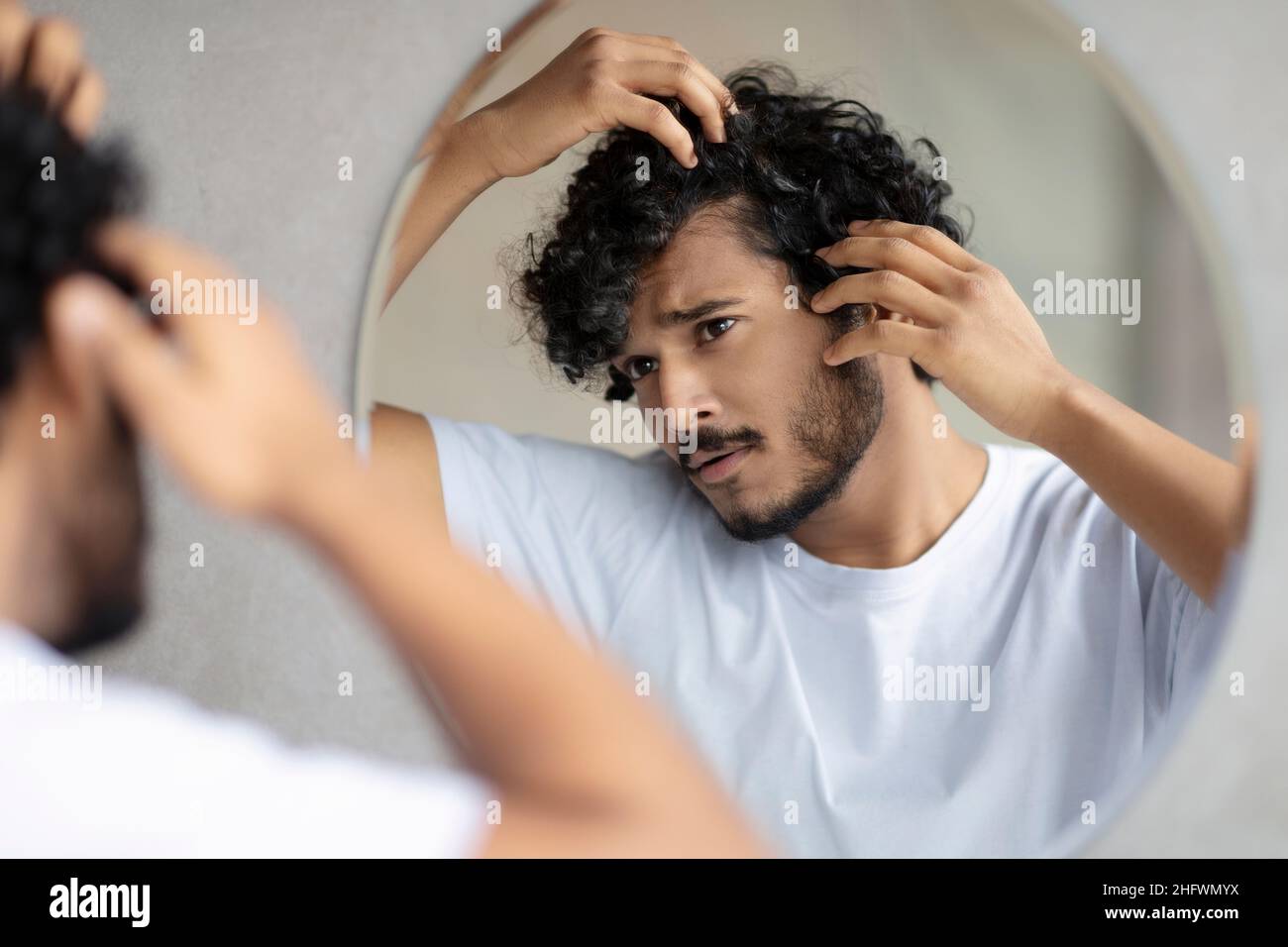 Trattamento di cura dei capelli. Ragazzo indiano preoccupato guardando il cuoio capelluto flaky nello specchio, esaminando i capelli grigi e hairloss problema Foto Stock