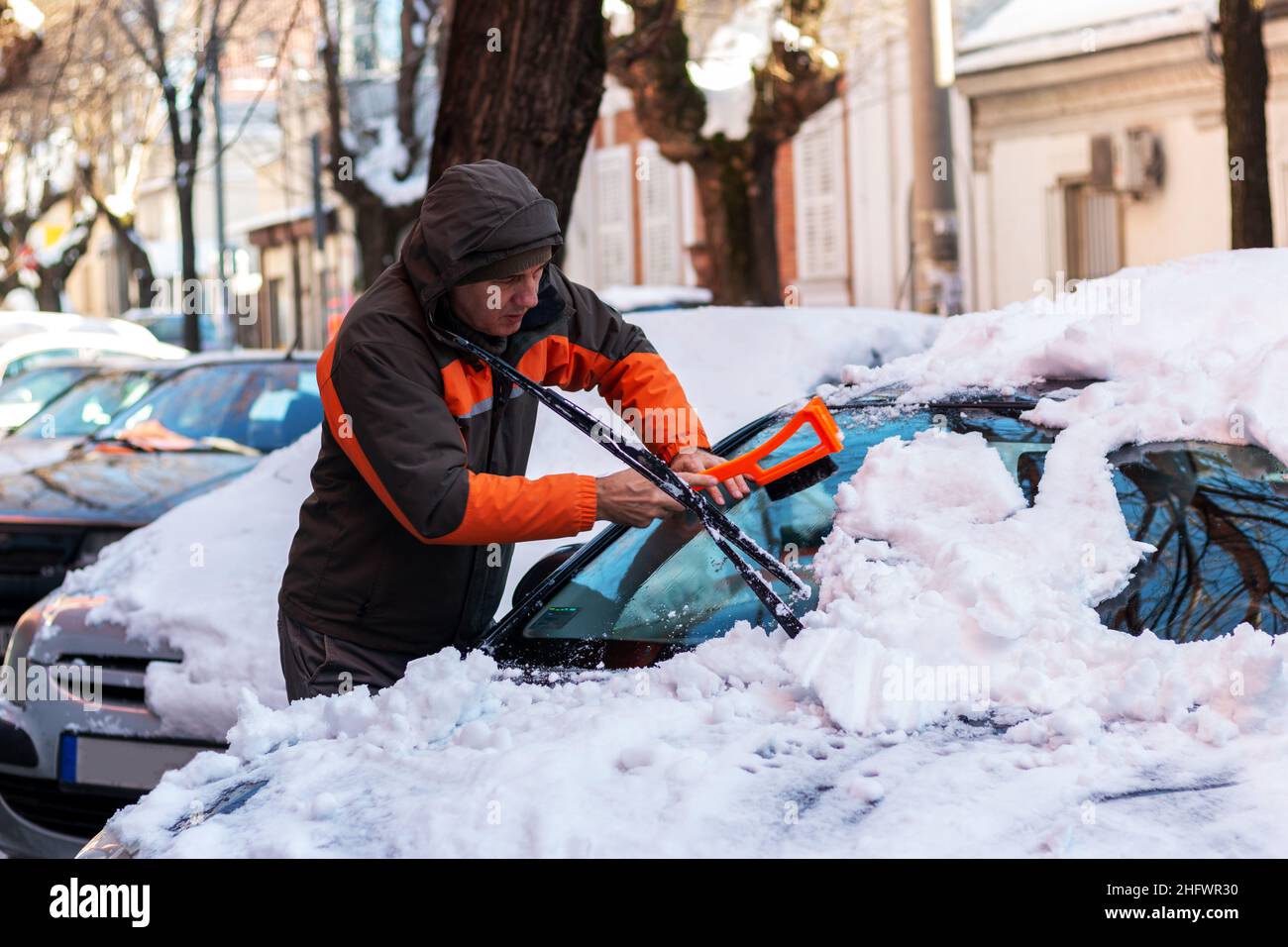 Uomo che pulisce il parabrezza dell'auto con raschietto e spazzola dalla neve e dal ghiaccio Foto Stock