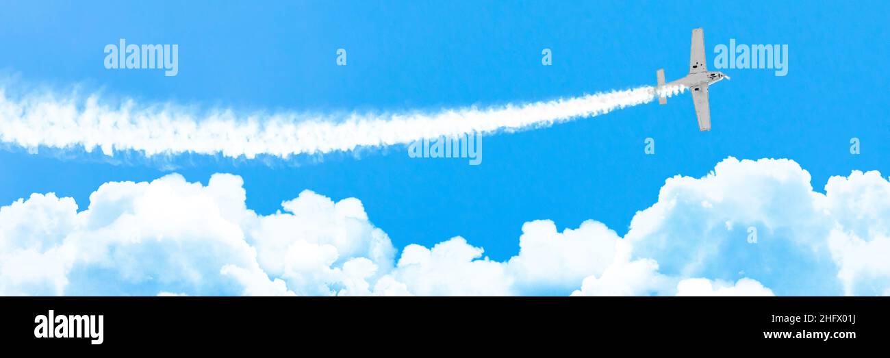 Velivolo motore leggero con una traccia di fumo bianco vola sulle nuvole di cumulo in estate, panorama Foto Stock