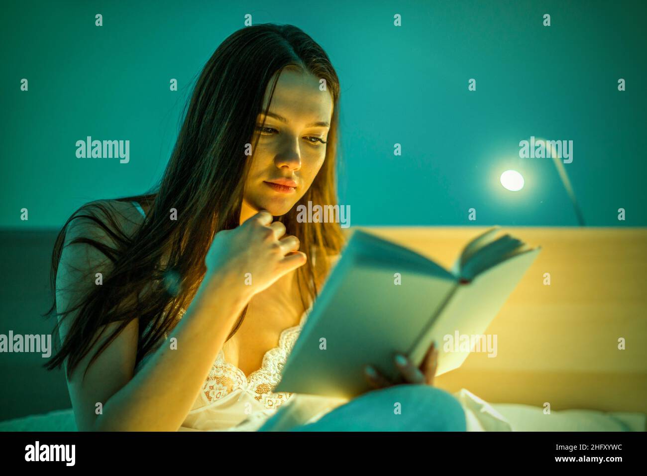 Relax. Una bella donna legge un libro con luci soffuse nella sua camera da letto prima di andare a letto. Autosviluppo. Letteratura. Foto Stock