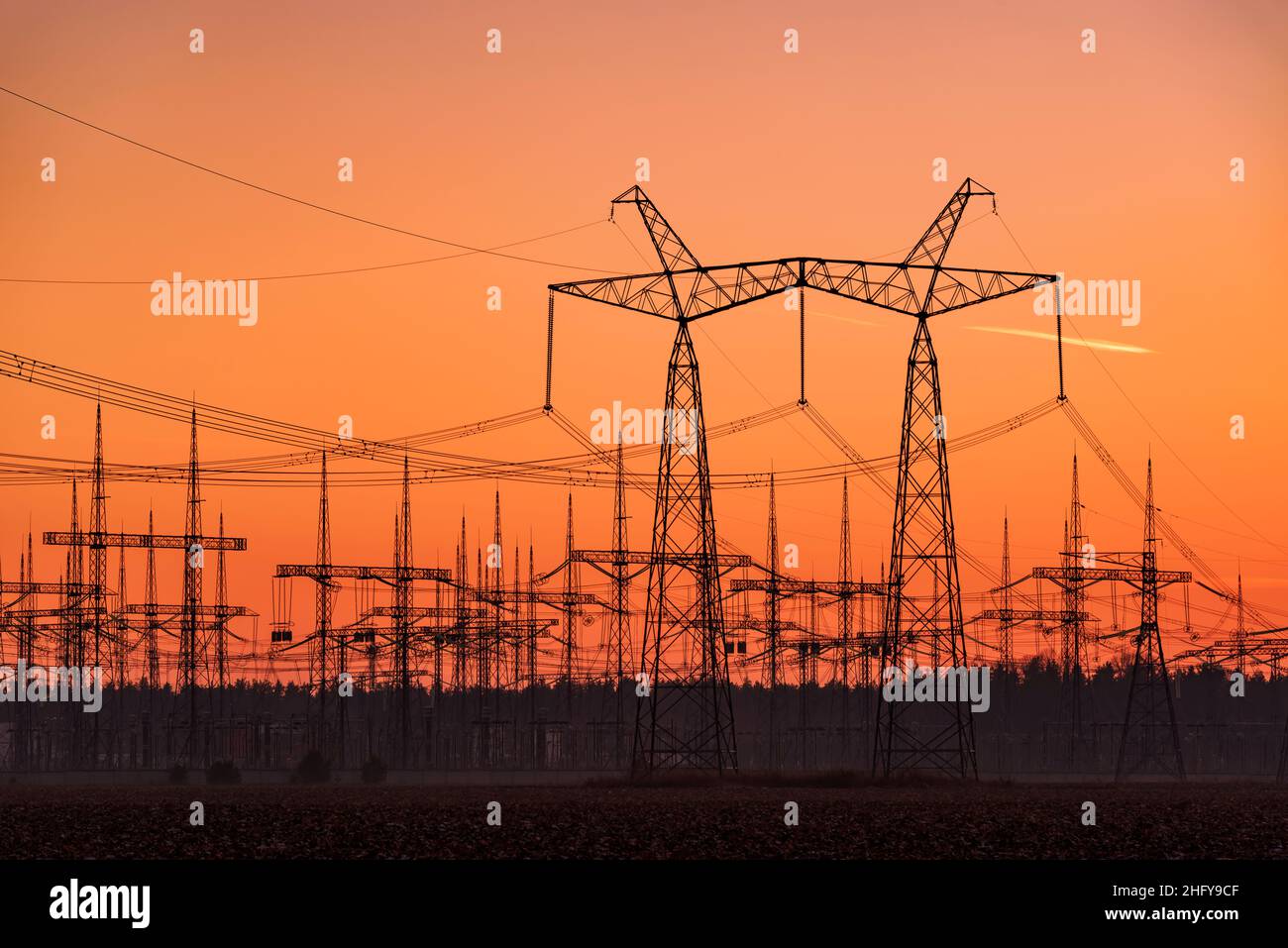 Sottostazione elettrica con sagome di molti piloni di linee elettriche al tramonto Foto Stock
