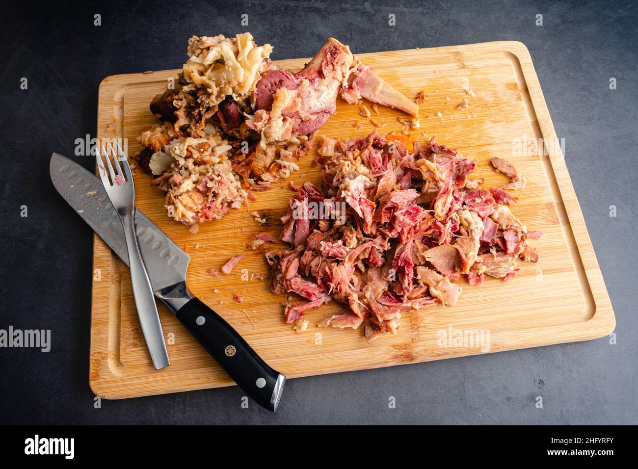 Rimozione della carne da un osso di cetriola bollito: Usando il coltello e la forchetta dello chef per rimuovere la carne da un'ossa di cetriola Foto Stock