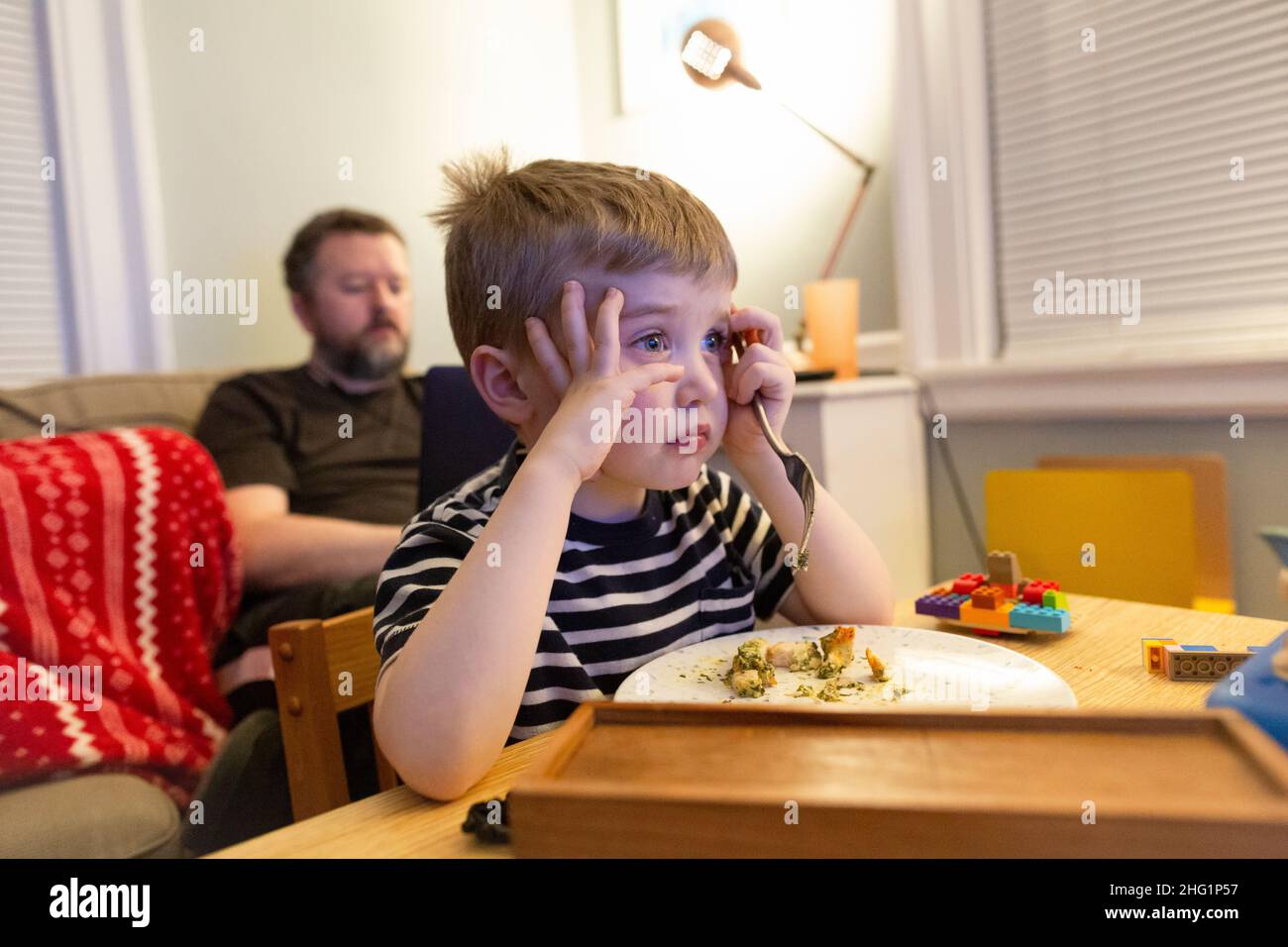 Adorable giovane ragazzo Watches Televisione mentre mangiano la cena casalinga-cucinata Foto Stock