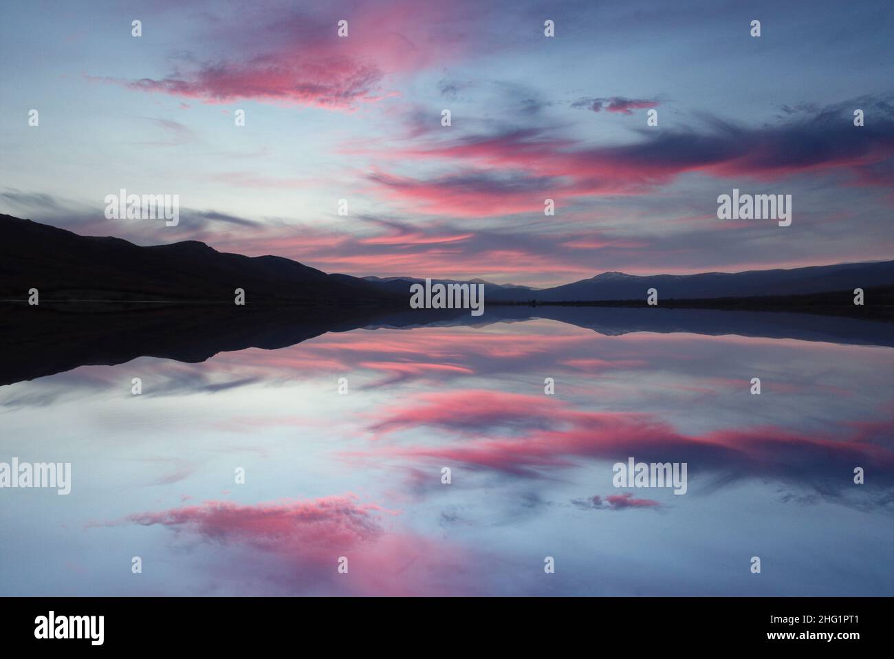 paesaggio di lago e montagne in tramonto rossastro con riflessi del cielo Foto Stock