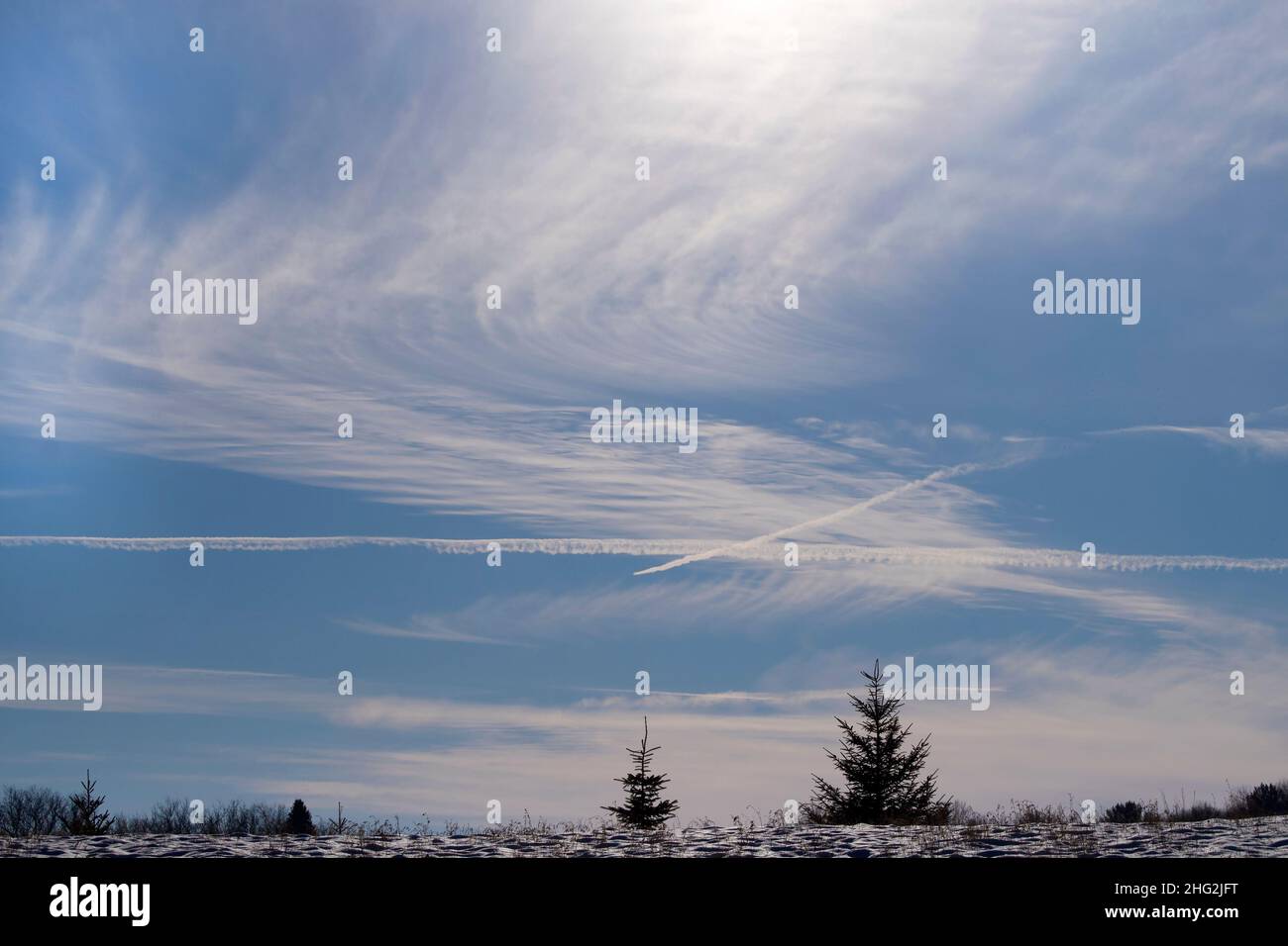 Cirrus e le nuvole di cirrostratus attraversate da jet aeroplano contravolgono la cima di una cresta. Foto Stock