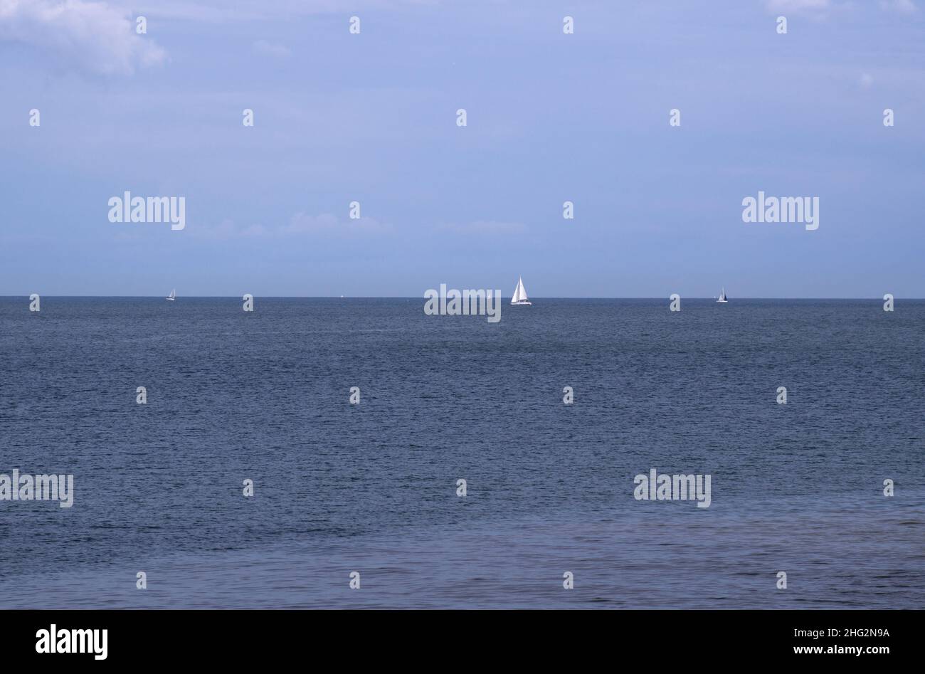 Bianco e blu - scena all'aperto sul lago Ontario con cielo blu, acqua blu, e una piccola barca a vela bianca sparsa nel lago all'orizzonte. Foto Stock