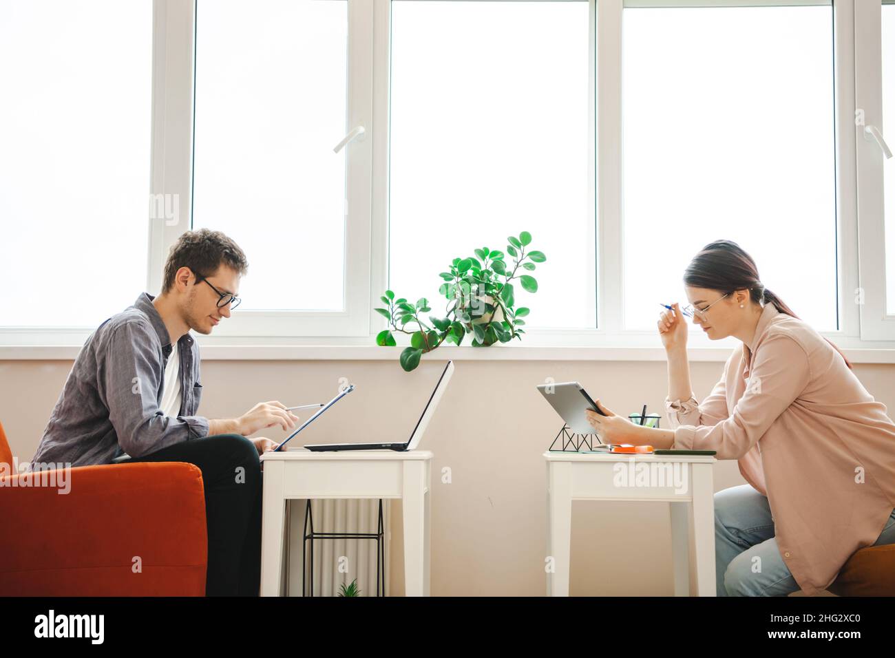 Uomo d'affari e donna che lavorano insieme utilizzando gadget come un tablet notebook. Lavorare da casa. Vista laterale. Foto Stock