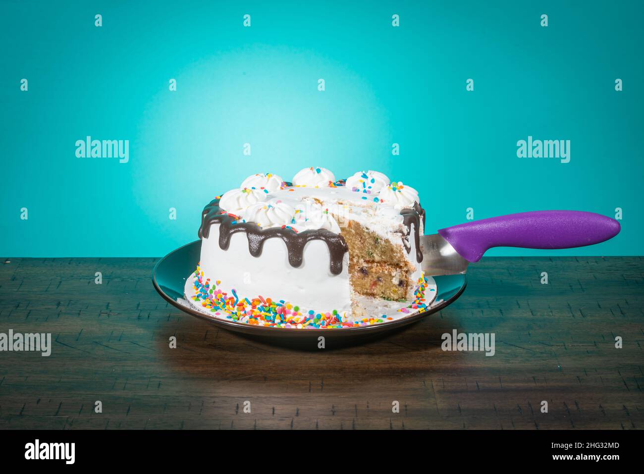 Una torta di compleanno, mancante di una fetta, ha un coltello viola che sporge dal suo lato. Foto Stock