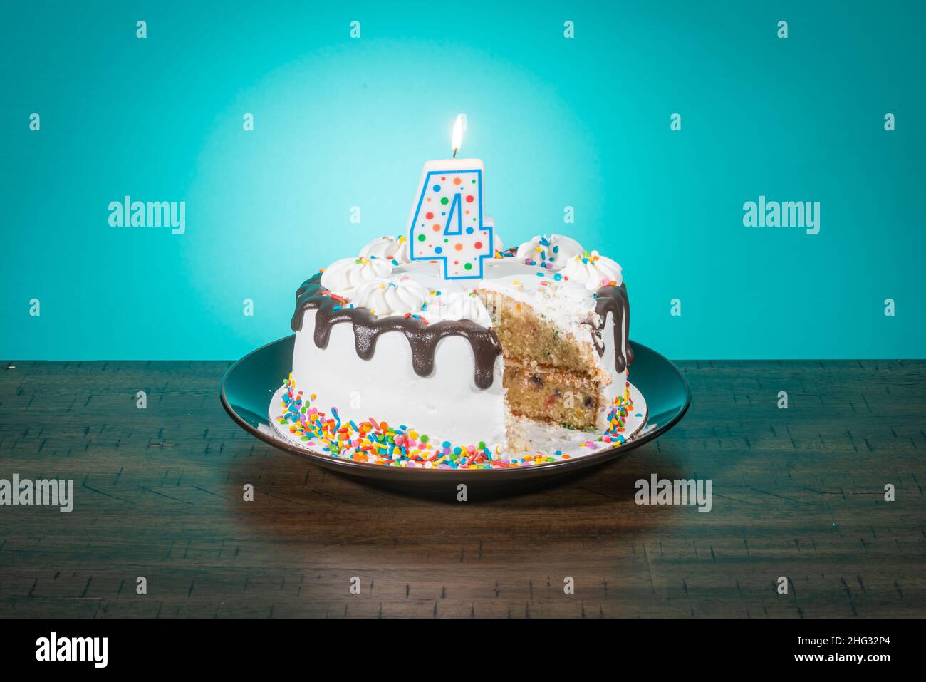 Una torta di compleanno, mancante di una fetta, porta una candela nella forma del numero 4. Foto Stock