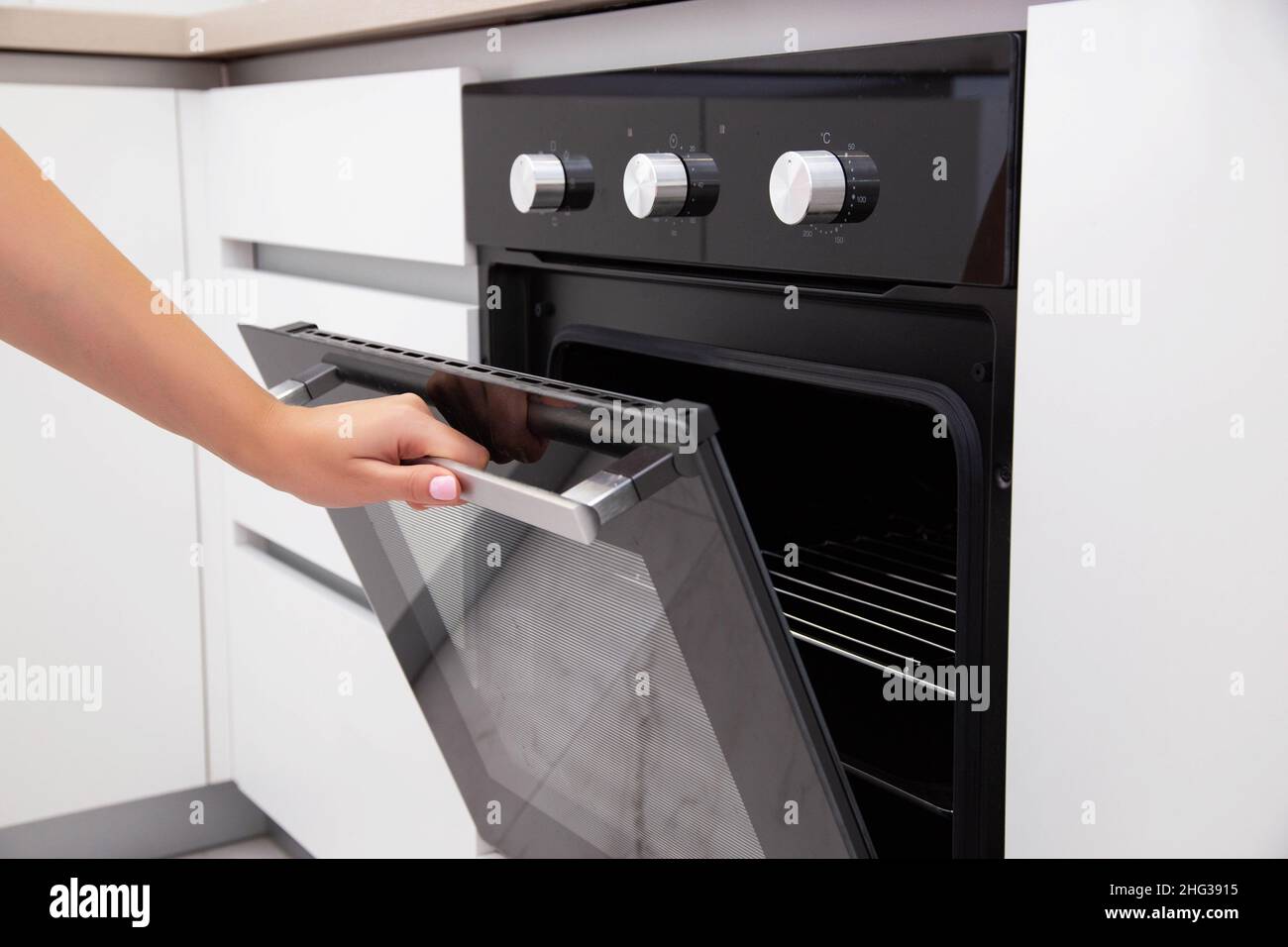 La mano di una donna apre la porta di un forno a convezione elettrica. Forno incorporato in cucina Foto Stock