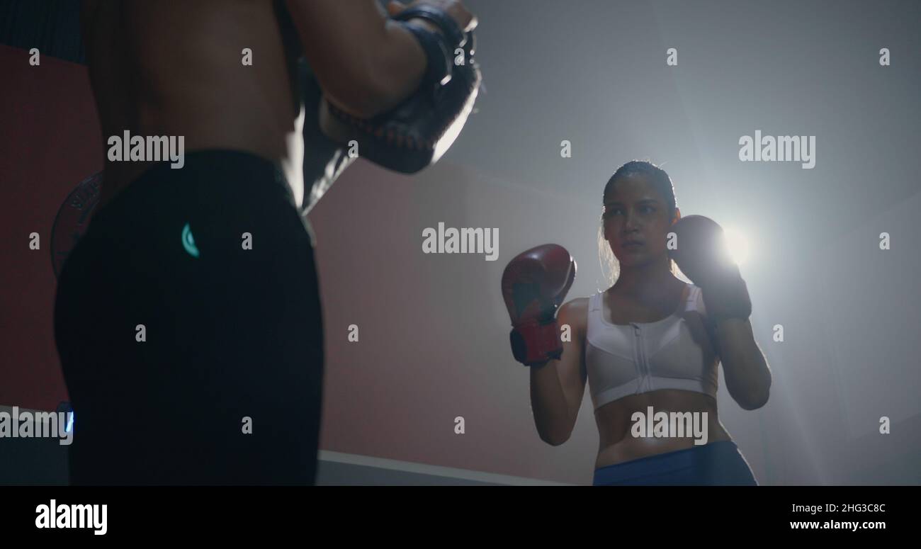 Asian bella giovane donna esercizio con allenatore a boxe guanti e auto-difesa lezione di punzonatura, femmina kickboxing formazione con maschio istruttore f Foto Stock