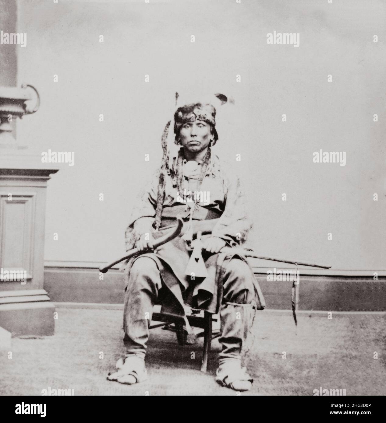 Foto d'epoca dell'uomo Winnebago, ritratto a tutta lunghezza, seduto, di fronte, con tomahawk e club in mano. USA. 1868-1880 Foto Stock