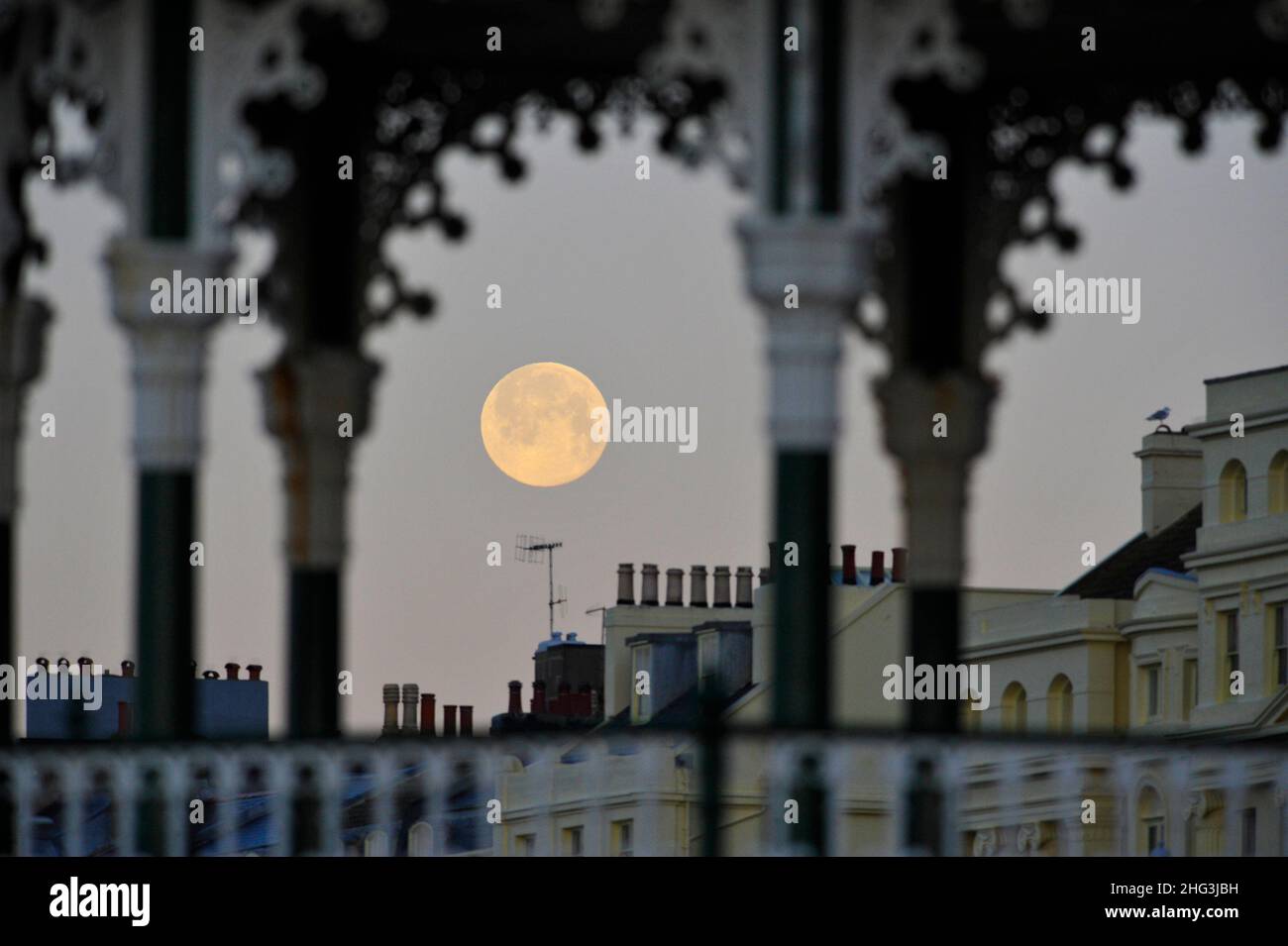Brighton UK 18th gennaio 2022 - il Wolf Moon affonda dietro il lungomare di Brighton e il banco di bandstand presto questa mattina . Tradizionalmente la prima luna piena dell'anno è conosciuta come la Luna del lupo . Credit Simon Dack / Alamy Live News Foto Stock
