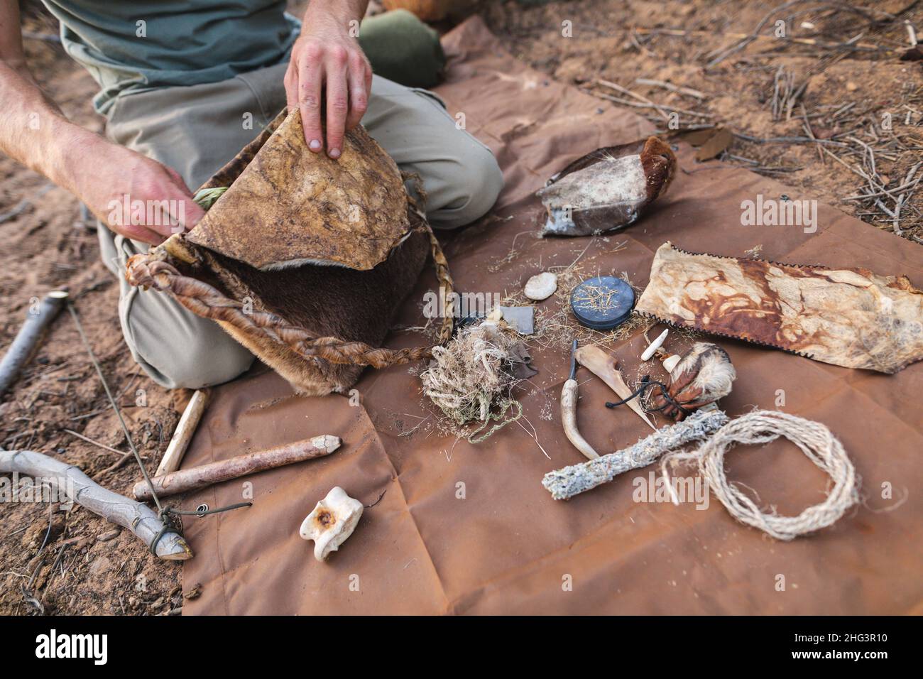 Sezione mediana del giovane sopravvissuto caucasico maschile con borsa in pelle fatta a mano inginocchiata da vari oggetti Foto Stock