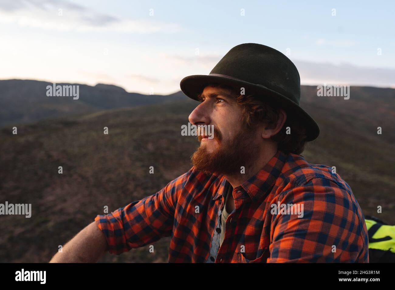 Giovane e premuroso uomo caucasico adventurer indossare cappello rilassante al tramonto Foto Stock