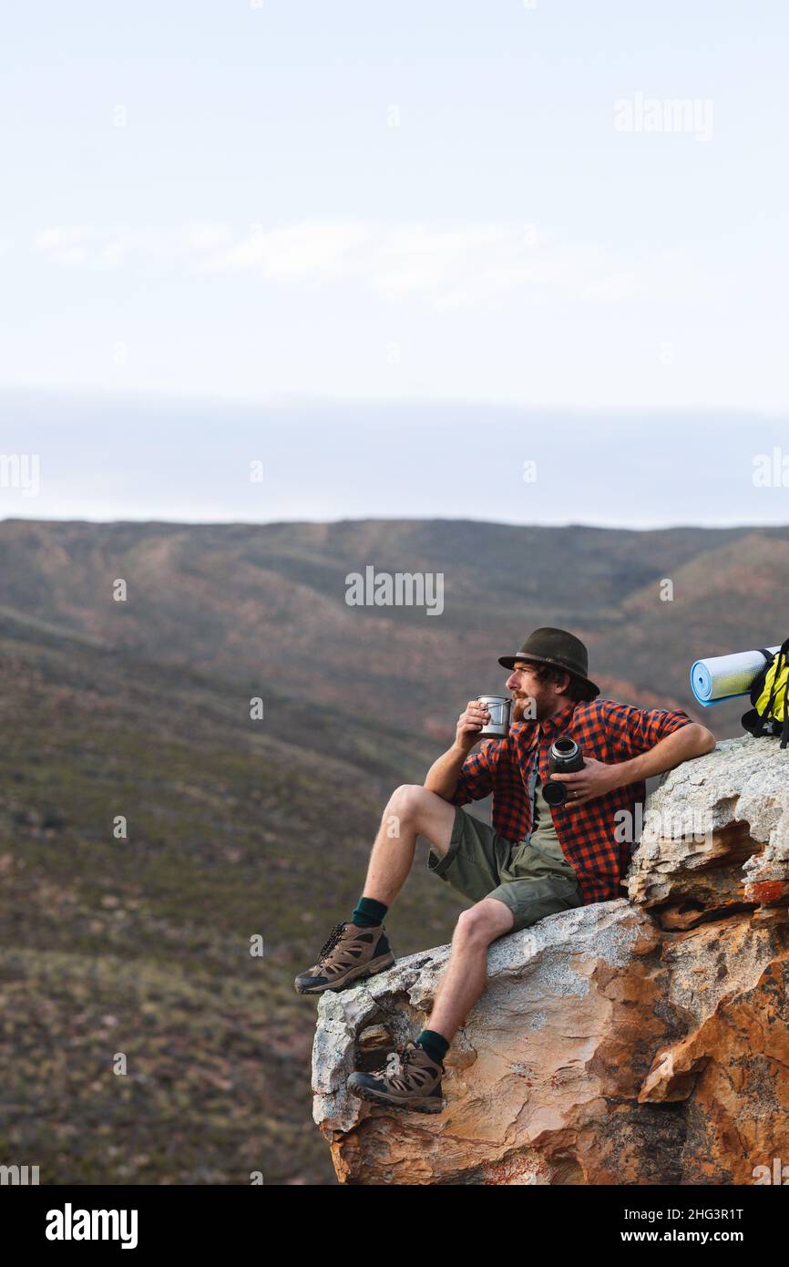 Giovane avventuriero caucasico maschio seduto con tazza su roccia in cima alla montagna con spazio copia Foto Stock