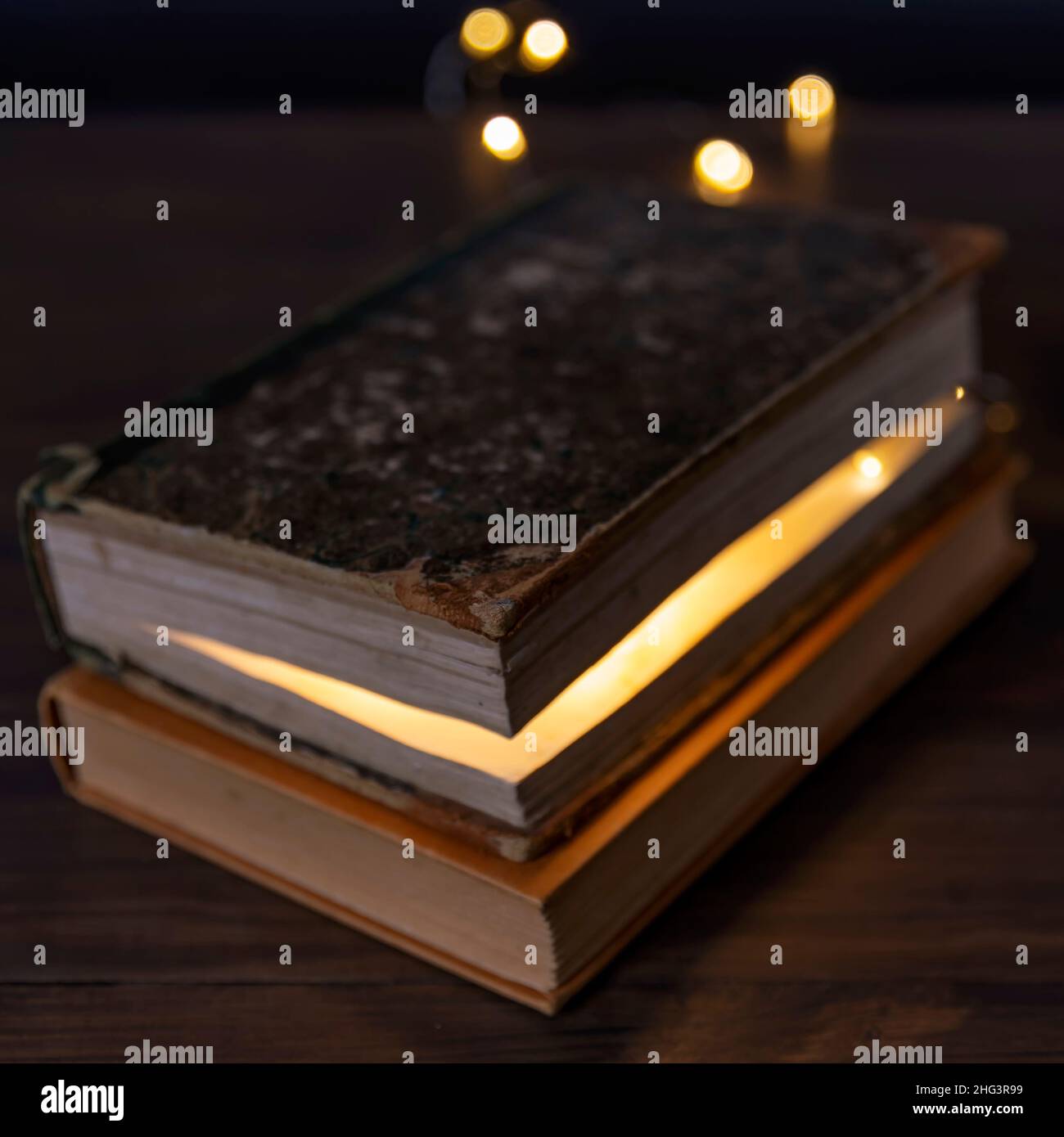 Due libri accatastati su un tavolo e all'interno di uno c'è una luce Foto Stock