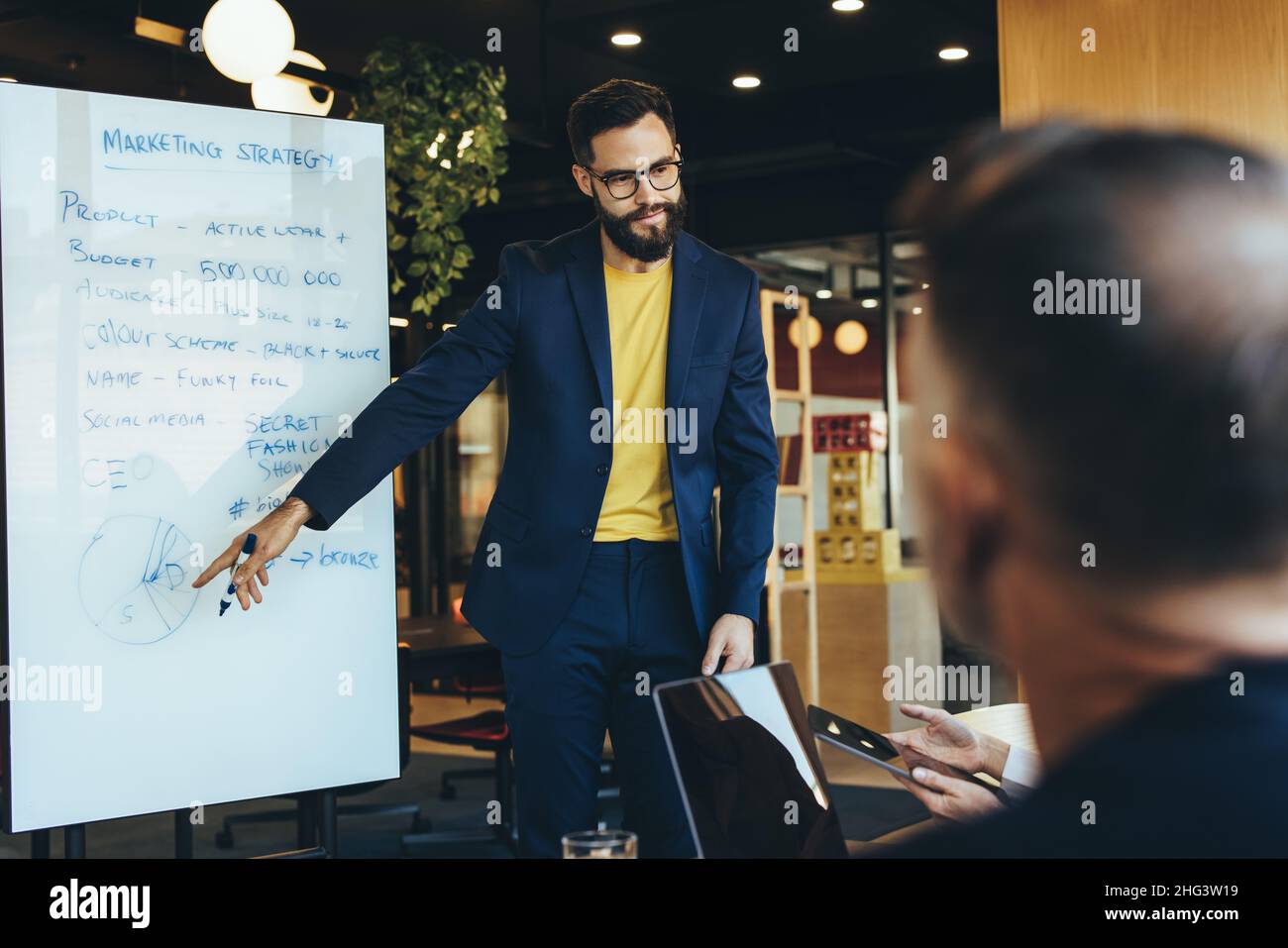 Giovane uomo d'affari che fa una presentazione durante un incontro con i suoi colleghi. Un manager aziendale fiducioso che discute le sue idee di marketing con il suo team Foto Stock