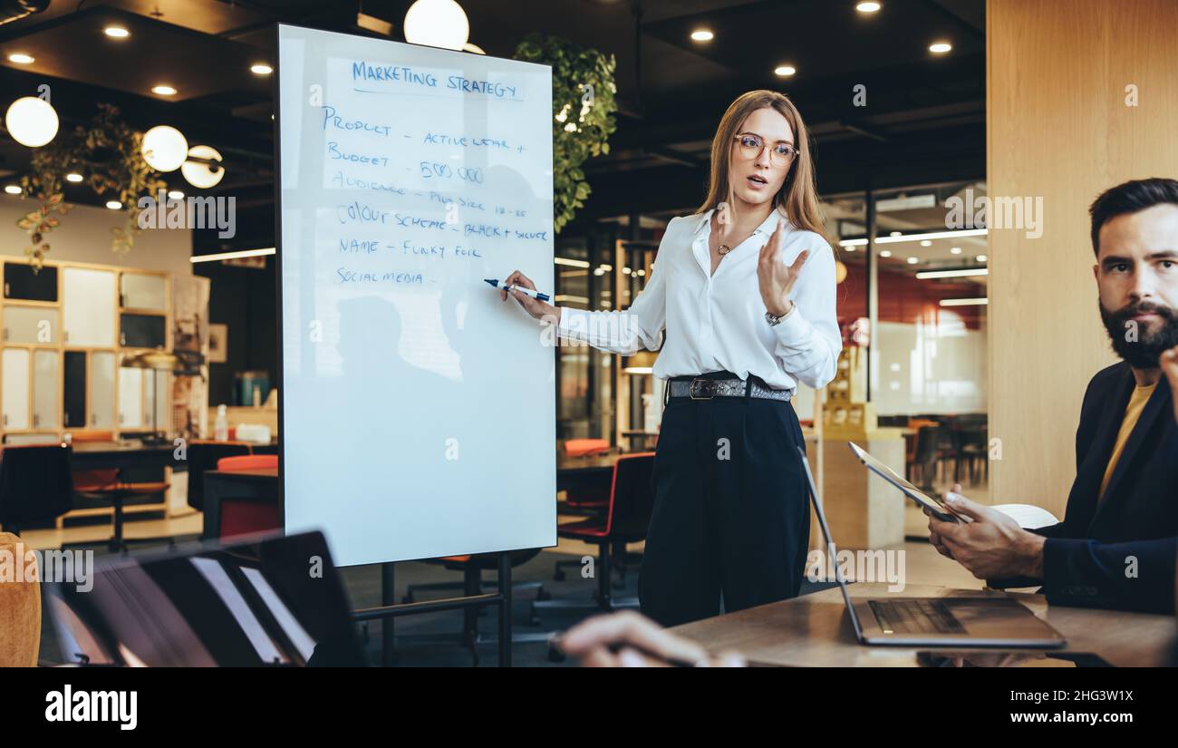 Manager che discute della sua strategia di marketing e delle sue idee con il suo team in un ambiente di lavoro moderno. Giovane donna d'affari fiduciosa che dà una presentazione durante un Foto Stock