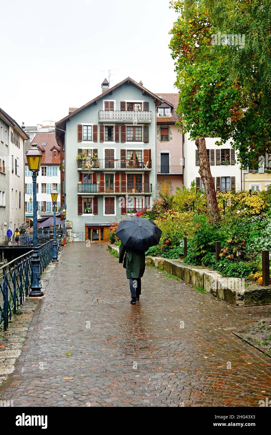 L'uomo cammina con un ombrello nero in una strada di Annecy, alta Savoia, Francia, sotto un giorno di pioggia di autunno Foto Stock