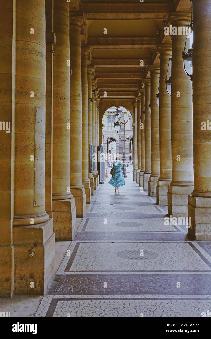 Donna cammina attraverso un corridoio con colonne e lanterne antiche in Rue de Rivoli, famosa e storica strada di Parigi, Francia Foto Stock