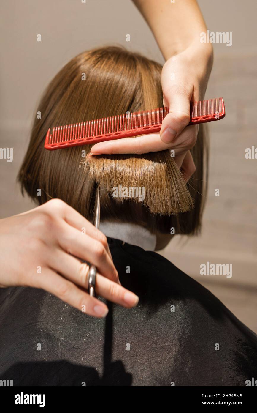 Closeup vista posteriore di ragazza di età preseena seduta in sedia in parrucchiere. Parrucchiere controllo del suo nuovo taglio di capelli Foto Stock