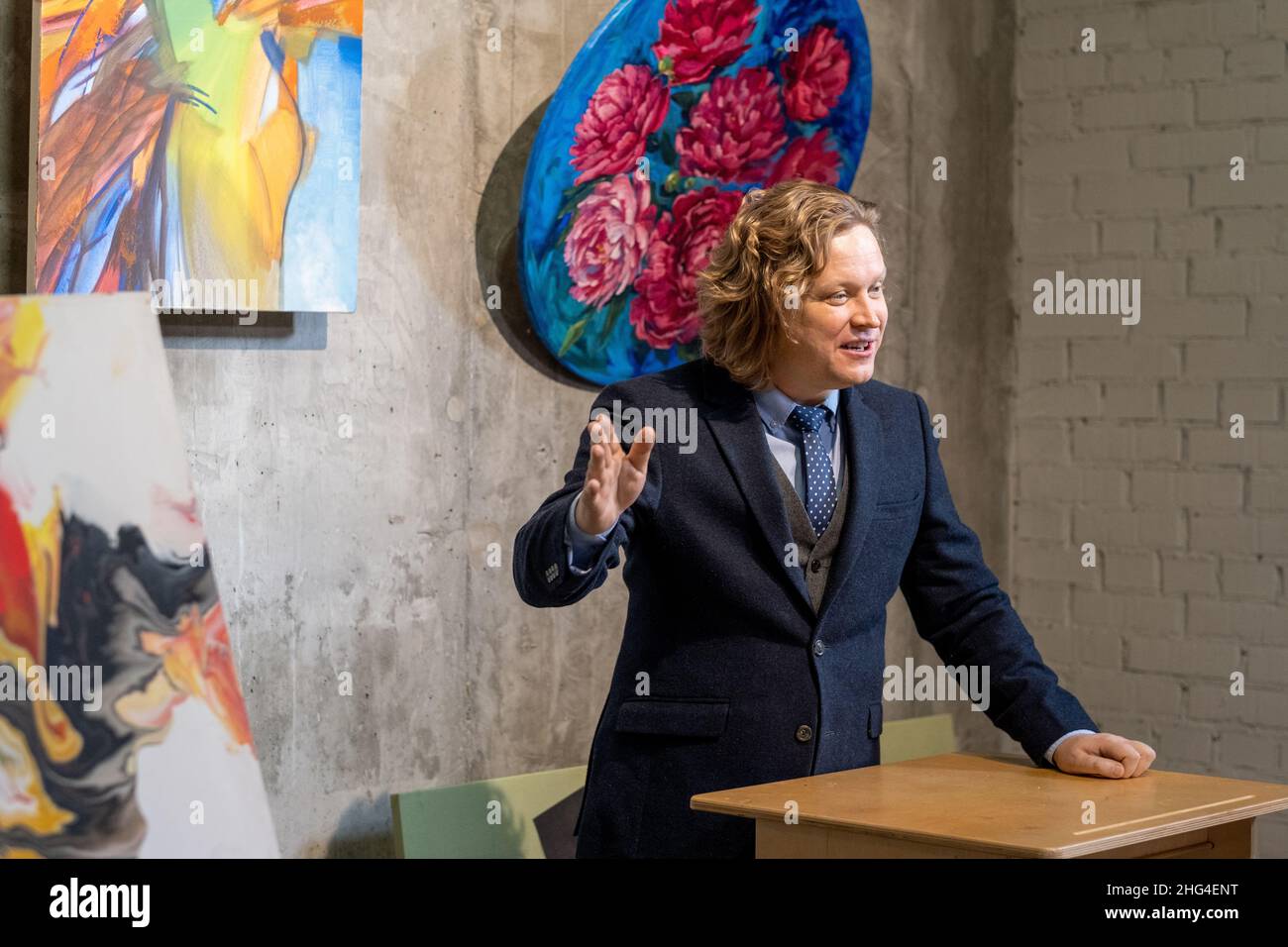 Auctioneer fiducioso in abito elegante in piedi da tribune, mentre presenta la collezione di opere d'arte per la vendita al pubblico Foto Stock