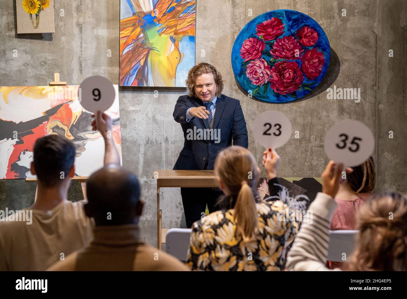 Maturo maschio auctioneer in abbigliamento formale in piedi da tribune e puntando a una delle persone con aste pagaie Foto Stock