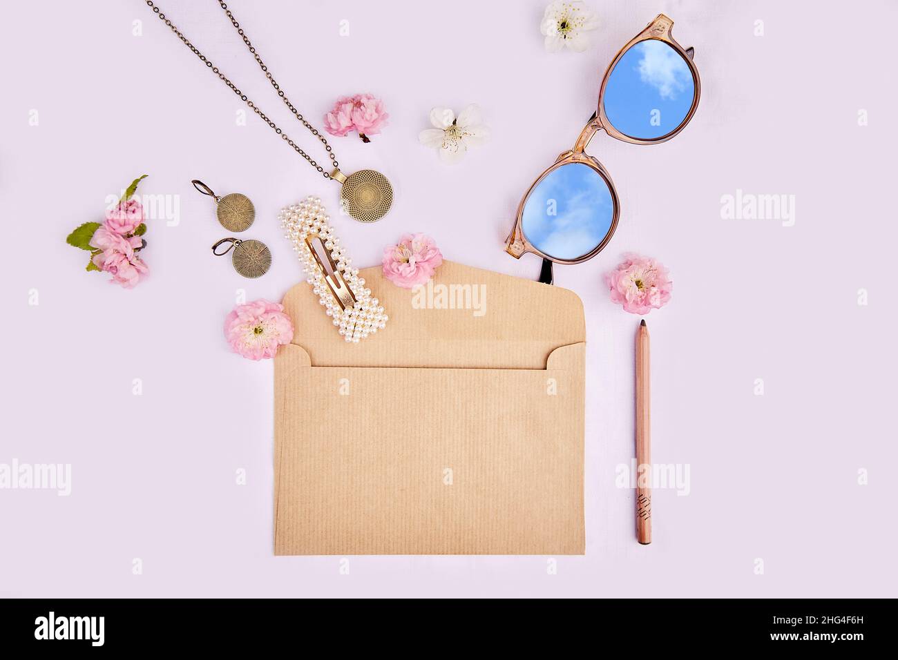 Splash di accessori donna da busta con fiori rosa. Occhiali da sole con riflesso del cielo, accessori, spilla, orecchini, pendente sul collo su fondo bianco in tessuto. 8 del concetto di marzo. Foto Stock